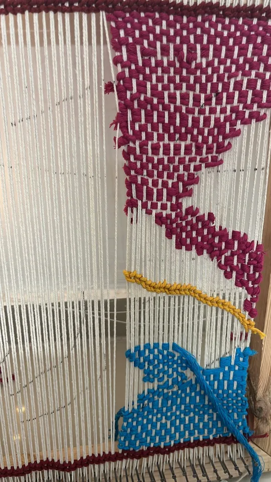The weave in progress with blue and magenta shapes growing on the warp.