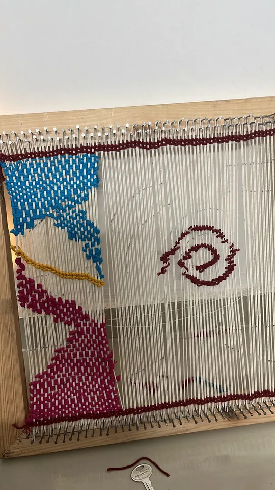 The weave in progress on a wooden frame loom, with the crimson spiral partly woven onto the cream warp.