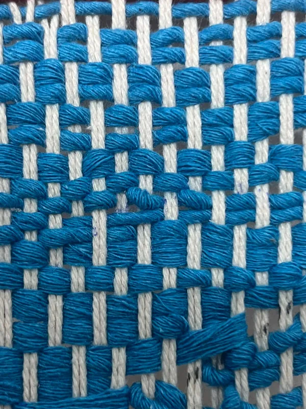 Close-up of bright blue yarn woven in a tight check over the cream warp.