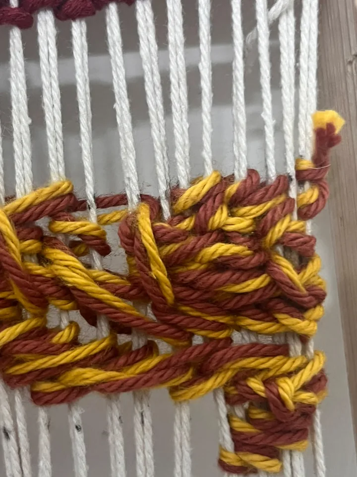 Close-up where gold and crimson yarn cross over the warp threads.