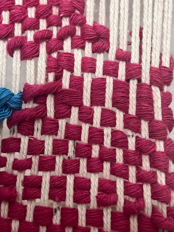 Close-up of magenta yarn woven in a loose basket pattern.