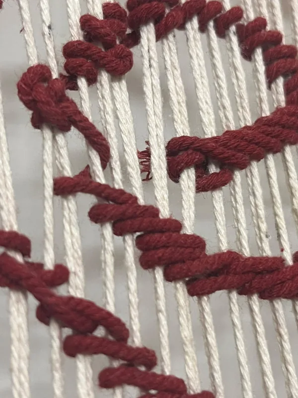Close-up of the crimson spiral woven in thick yarn over the cream warp.
